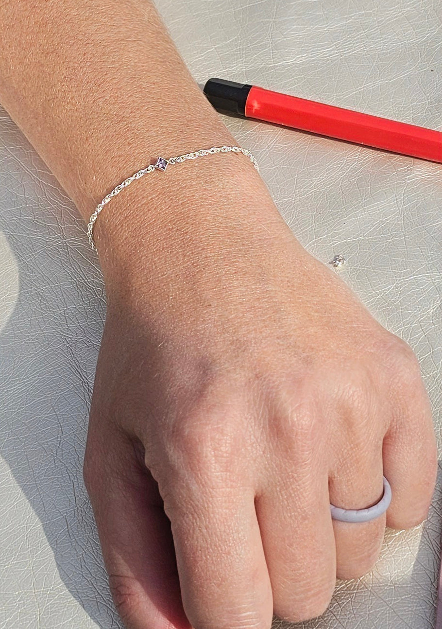Hand wearing a Sterling silver rope bracelet by intentionally linked permanent jewelry and ring on a light fabric background