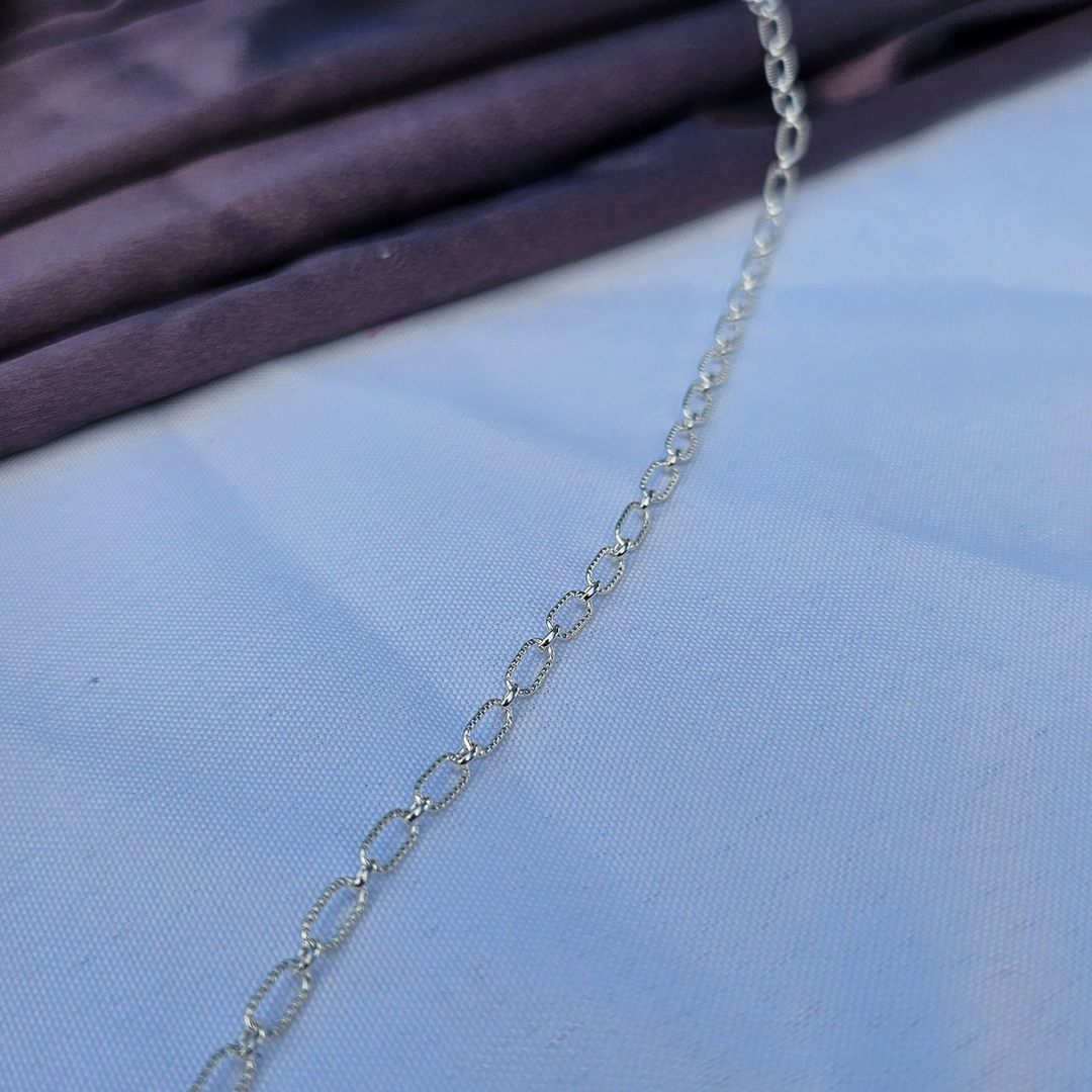 Close-up of Astraea sterling silver chain: textured oval link design catching light with subtle shimmer.