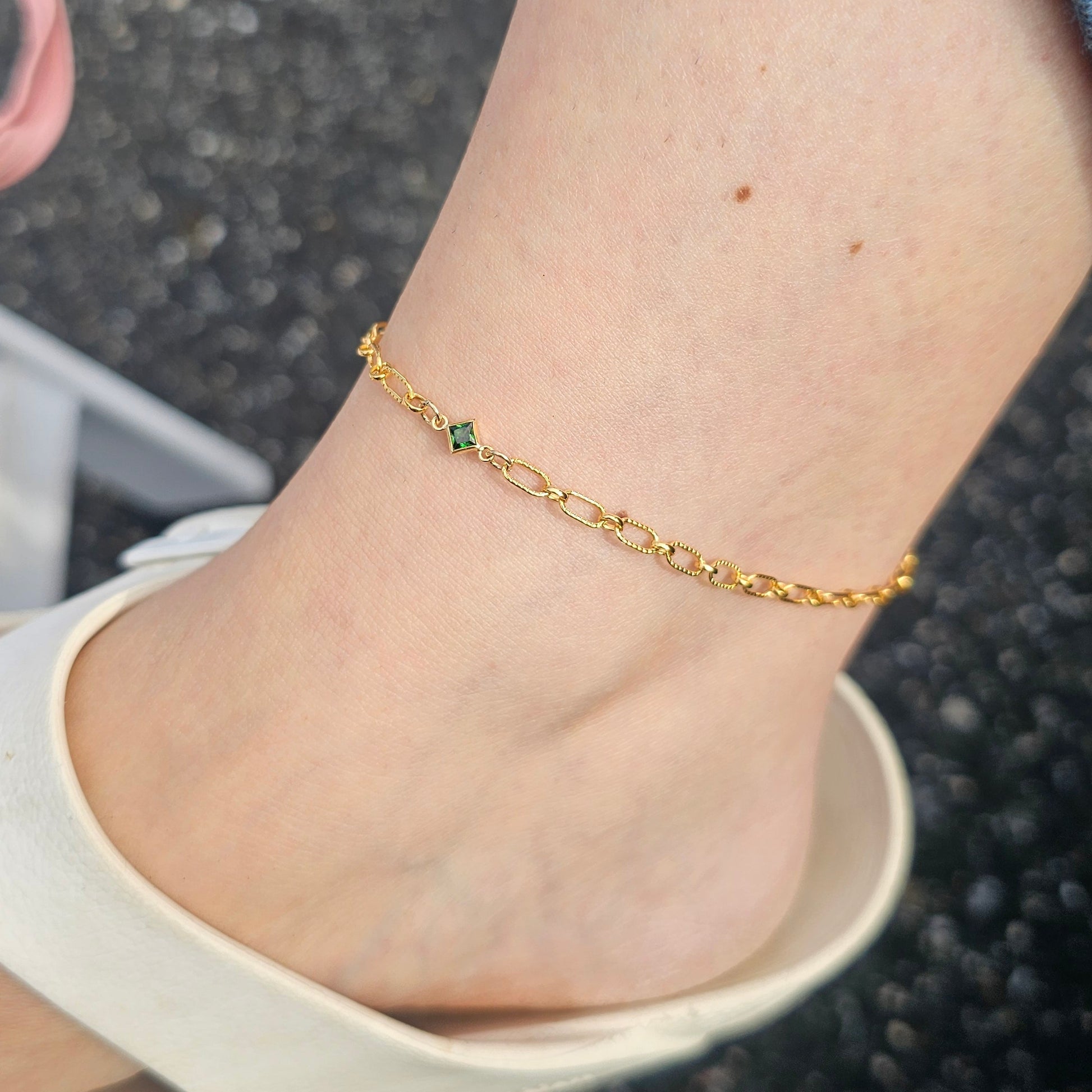Gold anklet with green stones on a person's ankle against a blurred background