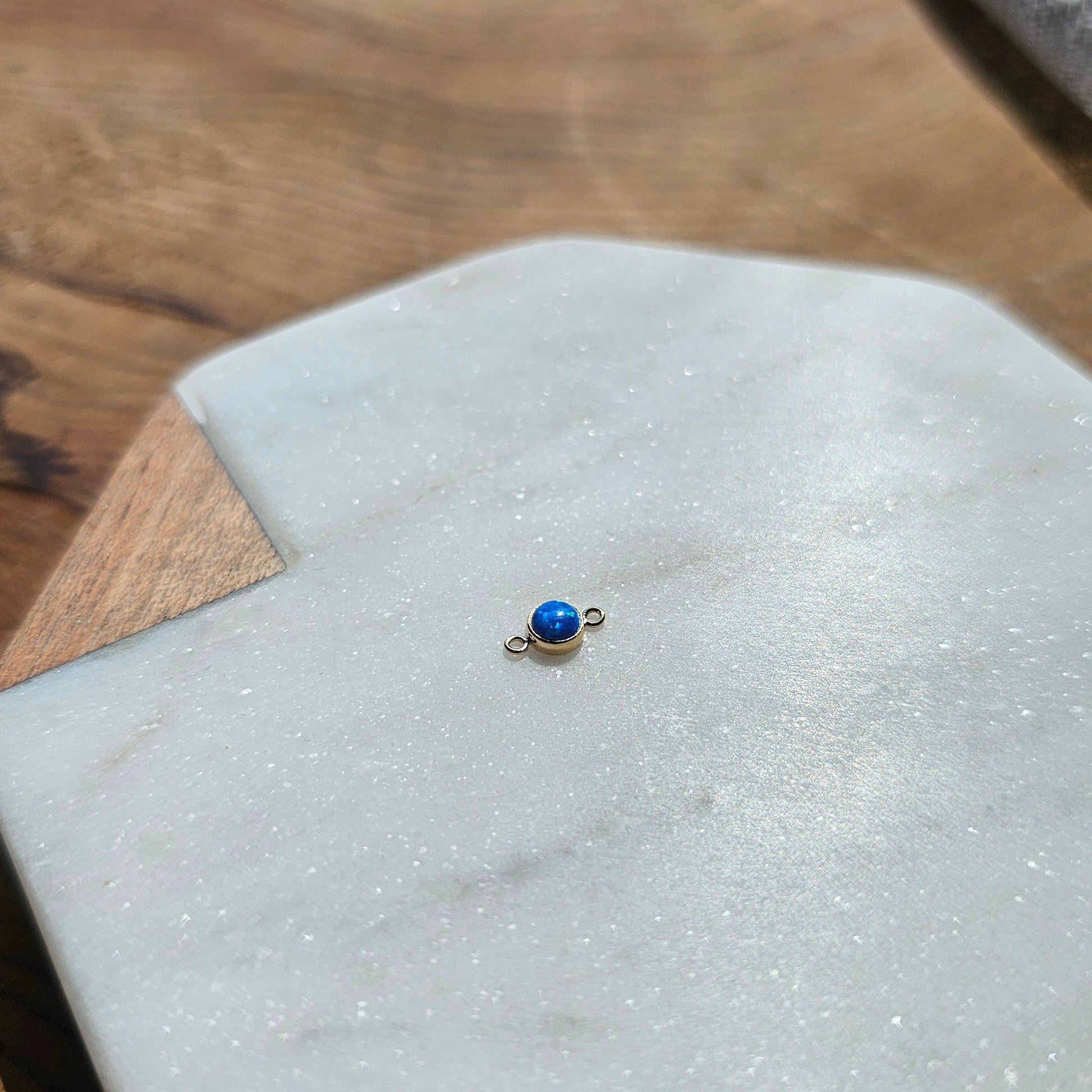 Small blue opal gemstone connector for Permanent Jewelry on a white stone surface with a blurred background