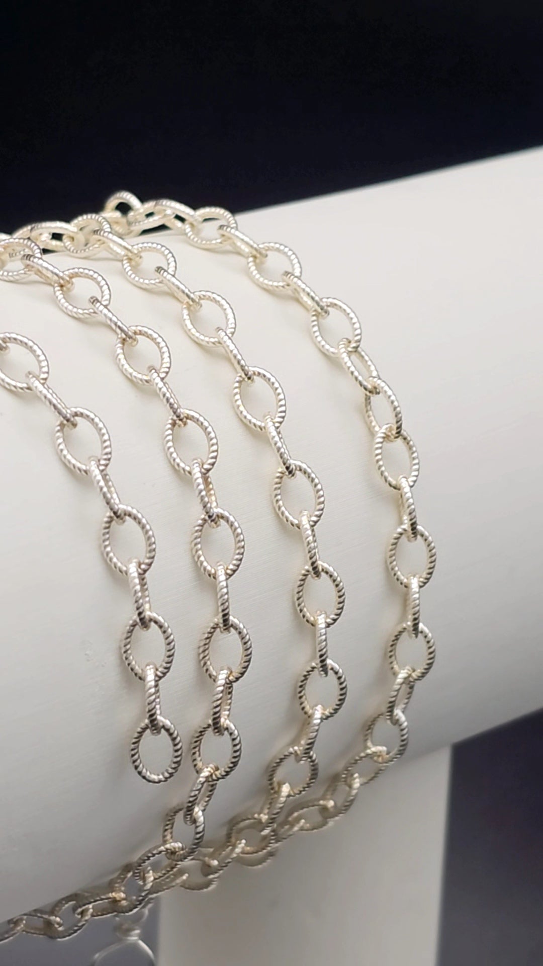 Sterling Silver fortis chain on a white stand with a dark background for intentionally linked permanent jewelry 