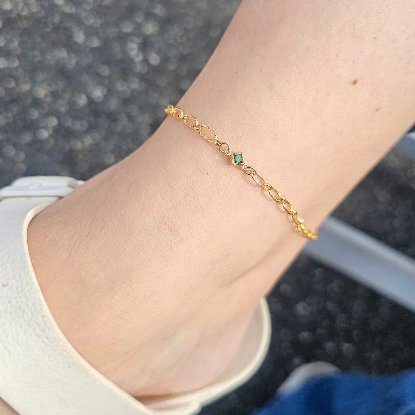 Gold bracelet with green stones on a person's wrist, wearing a white sandal.
