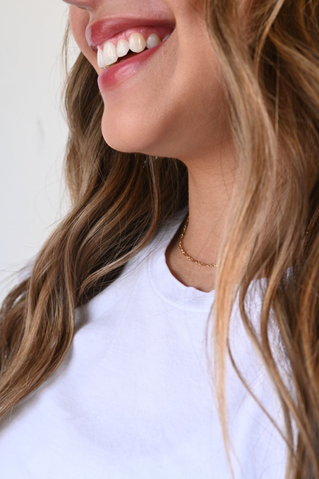 A smiling woman wears a dainty gold permanent necklace by Intentionally Linked Jewelry, captured in soft natural light. Promoting the new Canton, Baltimore permanent jewelry service page for intentional, everyday wear that never comes off.