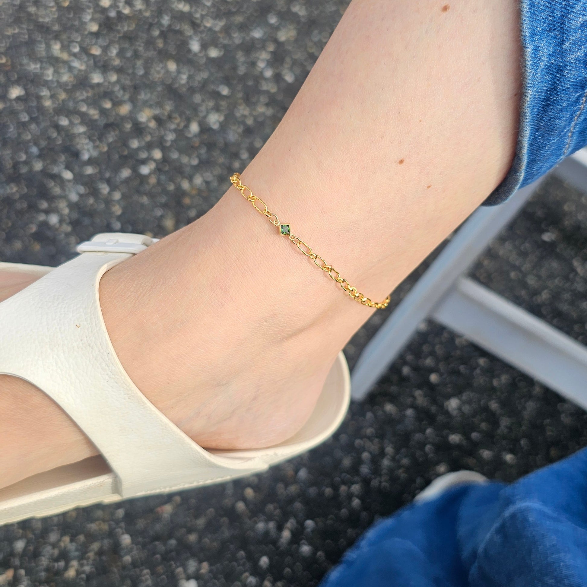 Close-up of a foot wearing a gold anklet on a pavement background