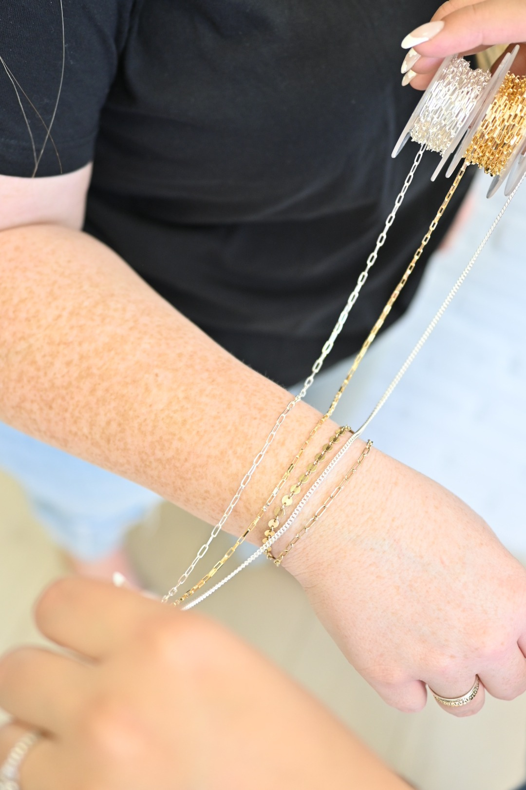 Close-up of a woman's hands holding spools of 14k gold filled chains at Intentionally Linked Jewelry's new permanent jewelry studio in Canton, Baltimore. The image highlights the variety of high-shine chain styles used for custom, permanent welded jewelry.