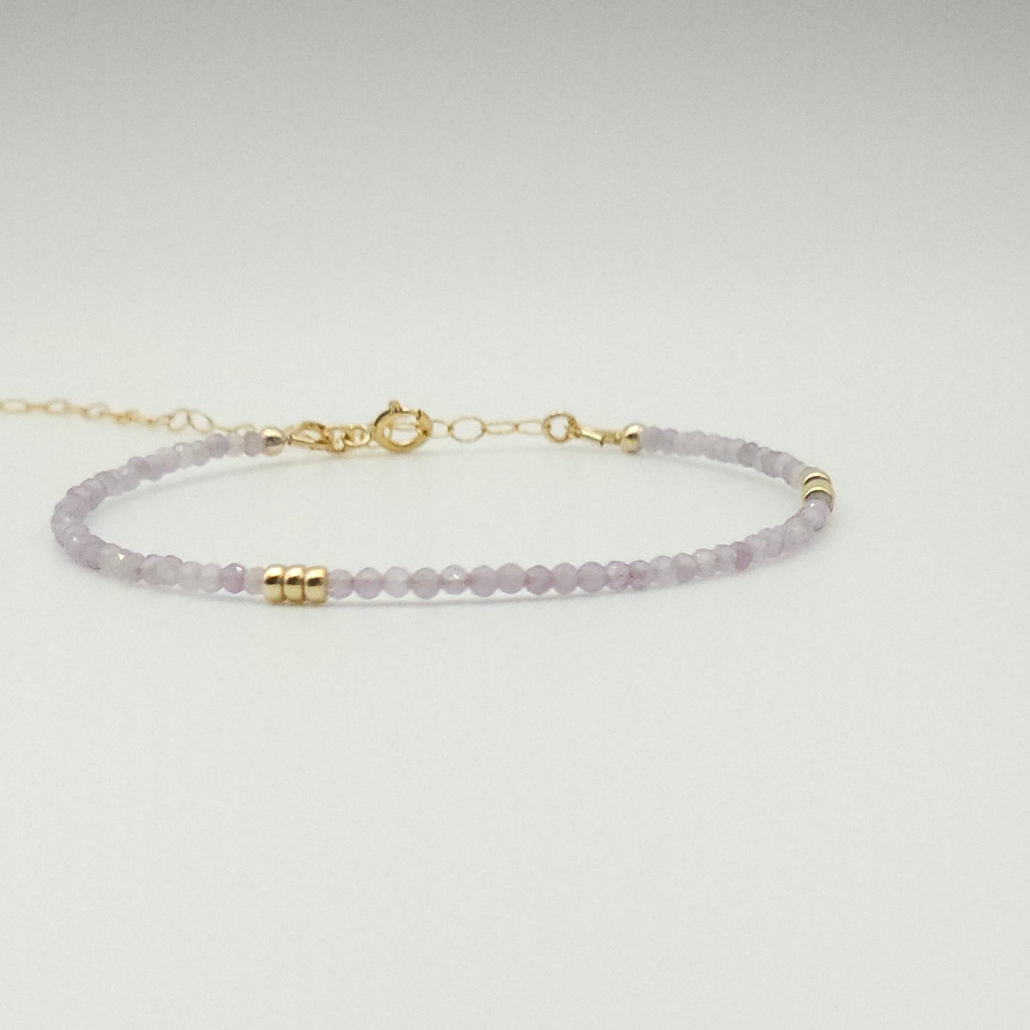 An adjustable bracelet with pink amethyst stones and gold accents, displayed against a white background.