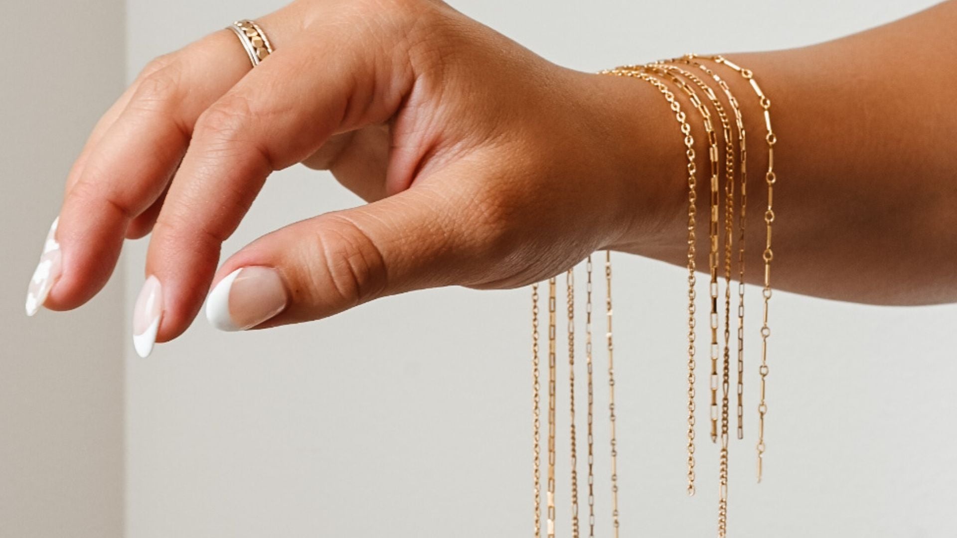 A woman's arm displays multiple gold filled permanent jewelry chains from Intentionally Linked Jewelry, draped elegantly over her wrist, ready for custom fitting. Each chain style reflects strength, connection, and timeless feminine energy—crafted for permanent wear and symbolic meaning